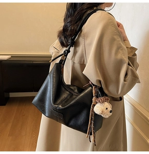 Detail of black leather hobo bag with teddy bear charm and knotted shoulder strap
