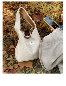 Close-up of white plush faux fur tote bag with OUR FAVE label on autumn leaves background