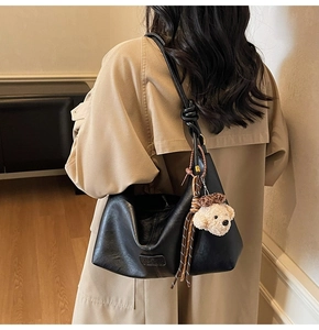 Detail of black leather tote bag featuring a knotted strap and a cute bear plush charm