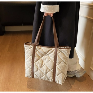 Detailed side view of off-white quilted tote bag with dark brown handles and trim