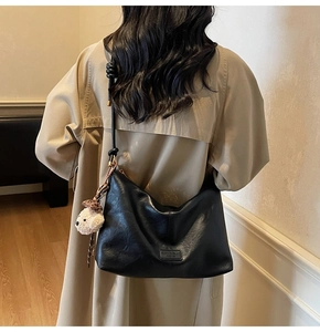 Detail of black faux leather tote bag with knot strap and white plush puppy charm