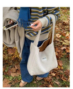 Detail of cream fleece tote bag with OUR FAVE label shown in outdoor autumn setting