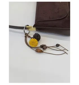 Detail eines Vintage-Anhängers mit Holzperlen und Stoffpompons an dunkelbrauner Wildledertasche