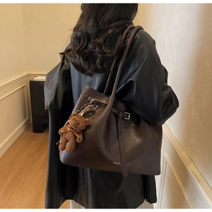 Detail of dark brown leather tote bag with logo and cute plush bear charm on strap