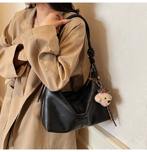 Detail of black leather hobo bag featuring knotted shoulder strap and plush bear charm