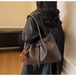 Detail of deep brown pleated tote bag with belt buckle and cute plush bear charm