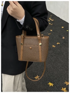 Dettaglio di una borsa tote intrecciata marrone con cinturini in pelle su foglie