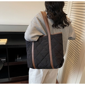 Detail of black quilted tote bag featuring brown leather straps and diamond patterns