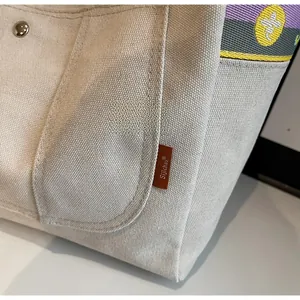 Detail of off-white canvas tote bag with metal buckle pocket and striped shoulder strap