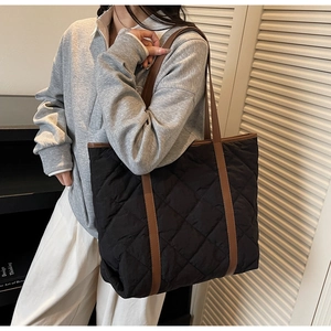 Detailed view of black quilted tote bag with brown handles worn on person shoulder