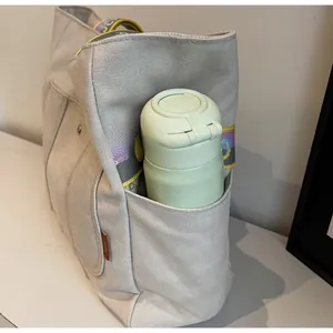 Detail view of canvas tote bag side pocket holding a green thermos water bottle
