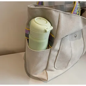 Detail view of the beige canvas tote bag showing side pocket holding a water bottle