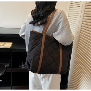 Detail of black quilted tote bag with large diamond stitching and brown leather strap