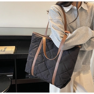 Detail of black quilted tote bag with diamond pattern and brown leather straps