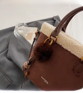 Détail d'un sac seau en daim marron avec bordure en polaire blanche et pompon