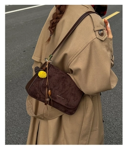 Außenaufnahme der braunen Wildledertasche mit Quasten-Detail am beigen Trenchcoat