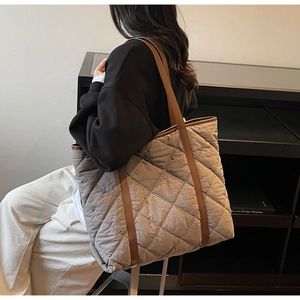 Detailed view of taupe quilted tote bag with brown leather straps worn by a model