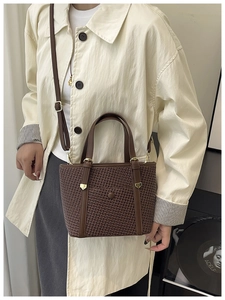Dettaglio borsa tote intrecciata marrone con manici in pelle su modella in cappotto