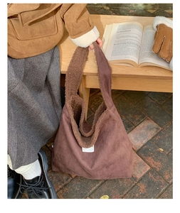 Detail of a brown suede tote bag featuring plush faux shearling trim and minimalist label