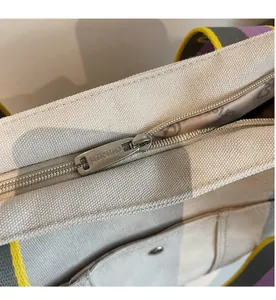 Detailed close-up of a sturdy metal zipper and colorful woven strap on a canvas tote bag