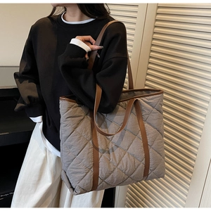 Detailed view of grey quilted tote bag with brown handles worn by a model in soft light