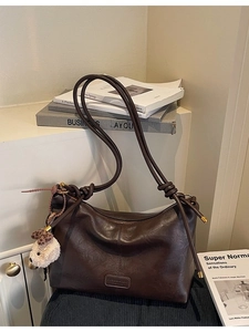 Vintage dark brown leather tote bag with a cute plush bear charm on a cream cabinet