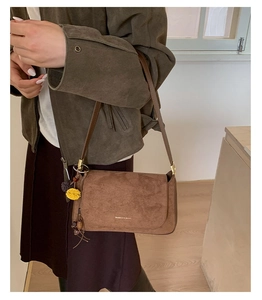 Detailaufnahme einer braunen Wildleder-Schultertasche mit Goldlogo und gelber Quaste