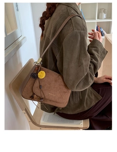 Braune Wildleder-Schultertasche mit dekorativem Bommel-Anhänger und minimalistischer Schrift