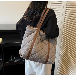 Detail of grey quilted tote bag featuring contrast brown straps on a fashion model