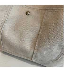 Detail of off-white canvas tote bag showing high-density texture and silver metal snap button
