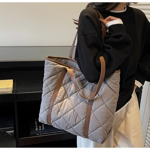 Close-up of a grey quilted tote bag with brown leather straps worn over the shoulder