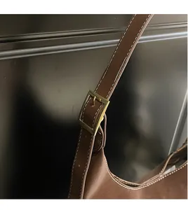Detail of brown leather bucket bag showing adjustable shoulder strap and gold metal buckle