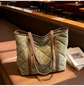 Detail of olive green quilted tote bag with brown leather handles in a cozy cafe setting