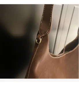 Close-up of brown leather bucket bag with white stitching and gold D-ring buckle detail
