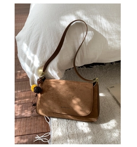 Detailaufnahme der braunen Wildledertasche mit zweifarbigem Plüsch-Anhänger auf weißem Teppich