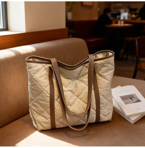 Detailed shot of beige quilted tote bag with brown leather handles on a vintage sofa
