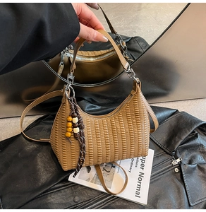 Close-up of brown pleated shoulder bag with wooden bead charm on black leather background