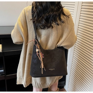 Detail of dark brown suede tote bag with ethnic tassel charm on beige sweater