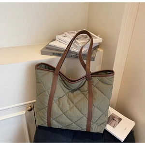 Detailed view of large olive green quilted tote bag with brown straps in a study setting