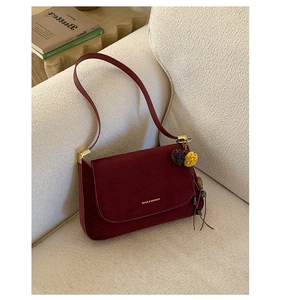Detail der weinroten Wildleder-Schultertasche mit goldener Hardware und Bommel-Anhänger