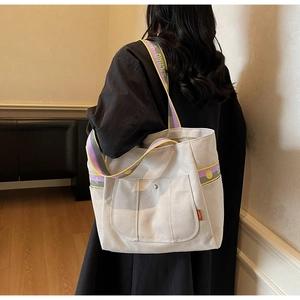 Detailed view of beige canvas tote bag with snap pocket and colorful webbing strap