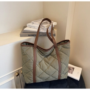 Detail of olive green quilted tote bag with brown faux leather handles on textured surface