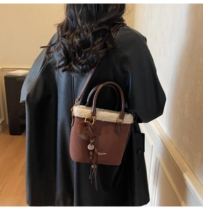Détail du sac seau en daim marron foncé avec bordure en peluche blanche et logo doré