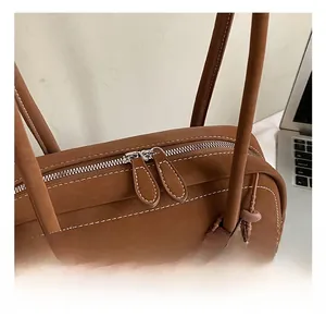 Close-up of brown suede Boston bag featuring silver dual zippers and woven pendant detail