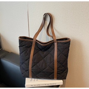 Detail of black quilted tote bag with brown leather handles on a white book