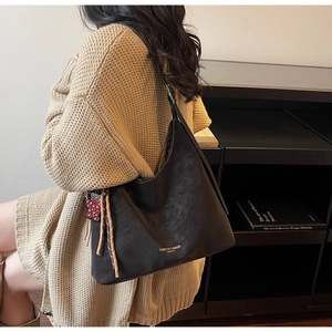 Close-up of retro black leather tote bag with leopard cat pendant and gold lettering
