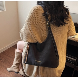 Detail view of black matte leather shoulder bag with gold embossed logo and metal buckle