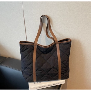 Detail of black quilted tote bag featuring brown leather trim and contrast stitching