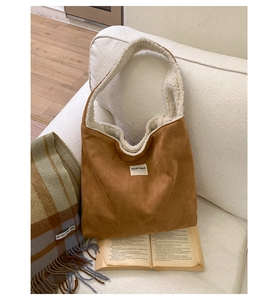 Detail of brown suede tote bag featuring sherpa lining and minimalist logo label on a sofa