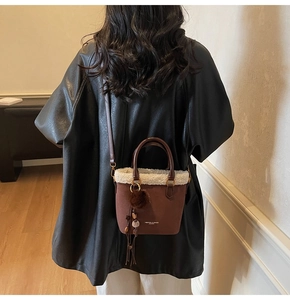 Détail du sac seau en daim marron avec bordure en fausse fourrure blanche et lettrage